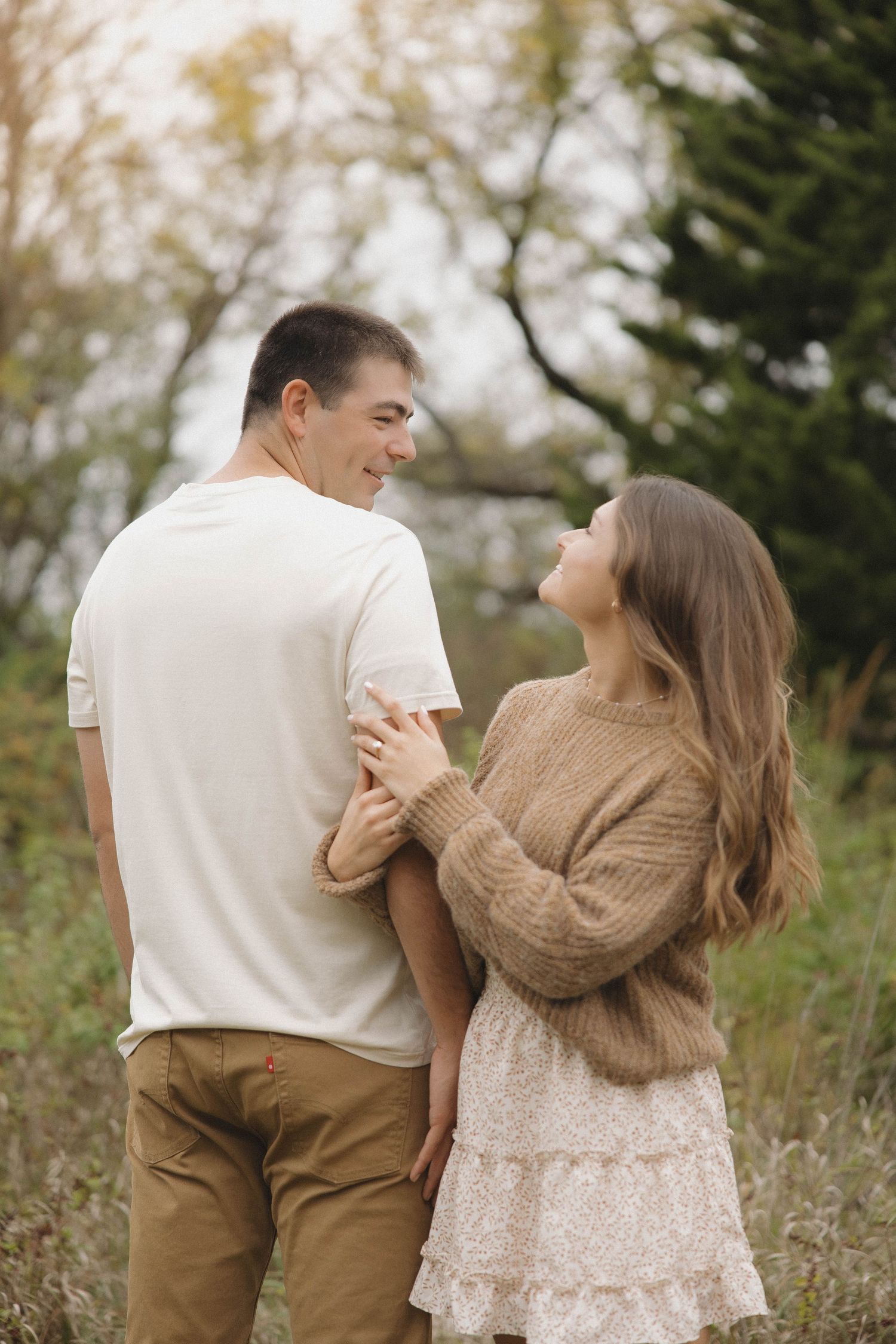 A couple in casual autumn attire sharing a joyful moment together outdoors among trees.