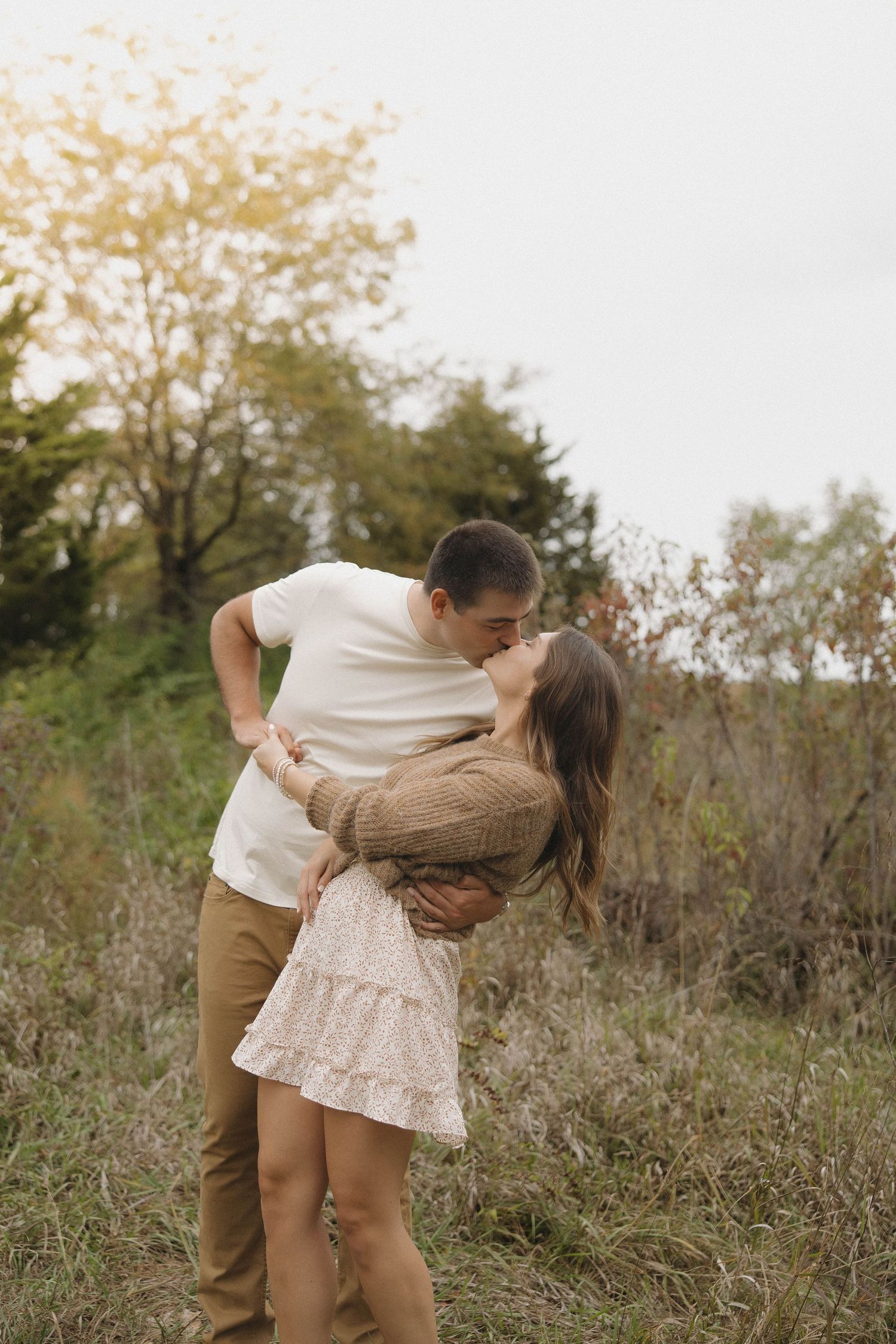 A couple dances playfully together in a field of tall grass and wildflowers during golden hour.
