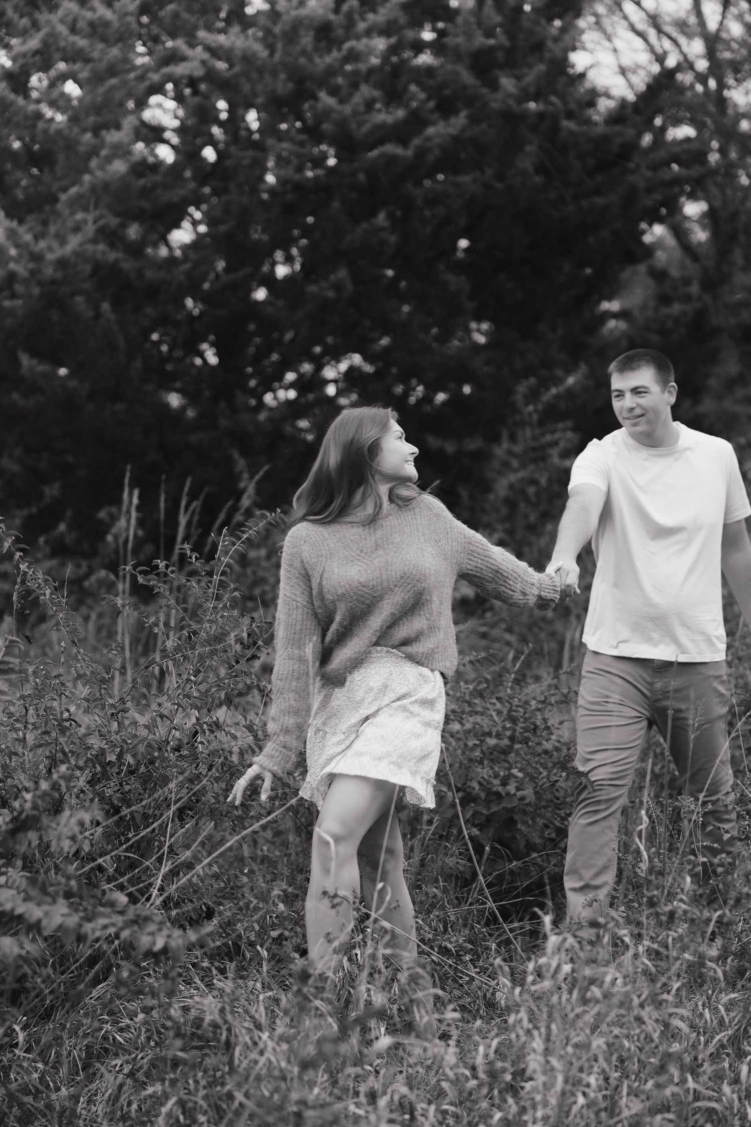 Black and white photo of a couple sharing joyful moments in a meadow with tall grass.