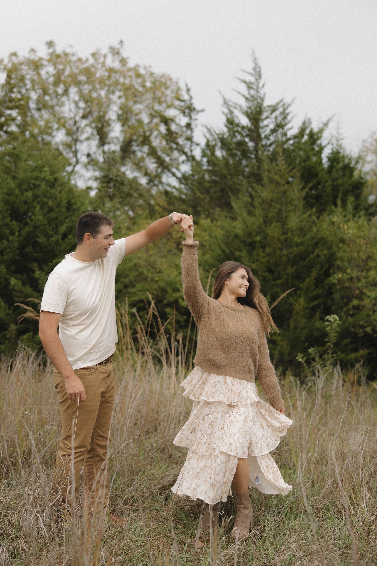 A couple dances together in a rustic field surrounded by autumn foliage and tall grass.