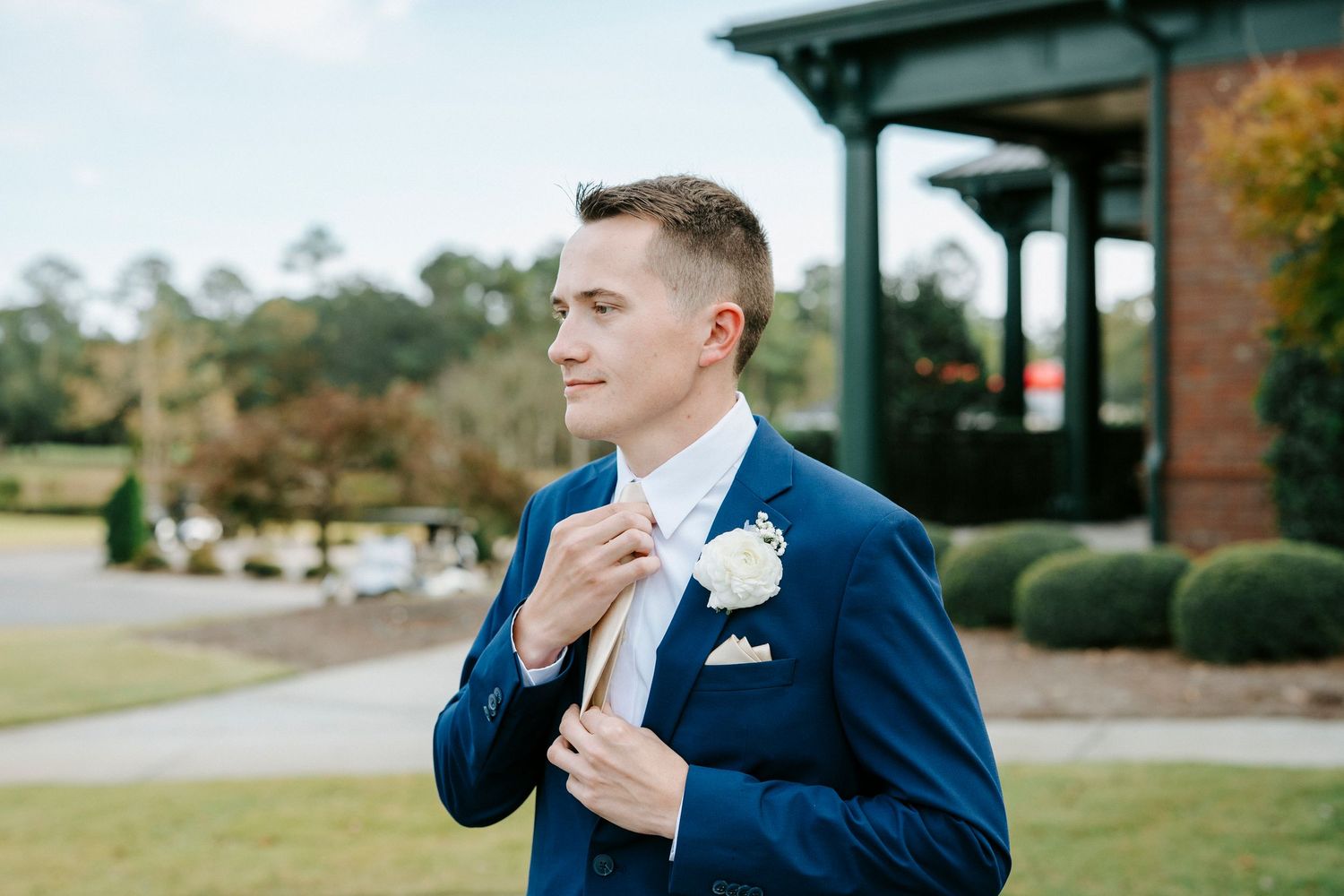 Someone in a navy blue suit wipes away tears during an emotional moment at an outdoor wedding ceremony.