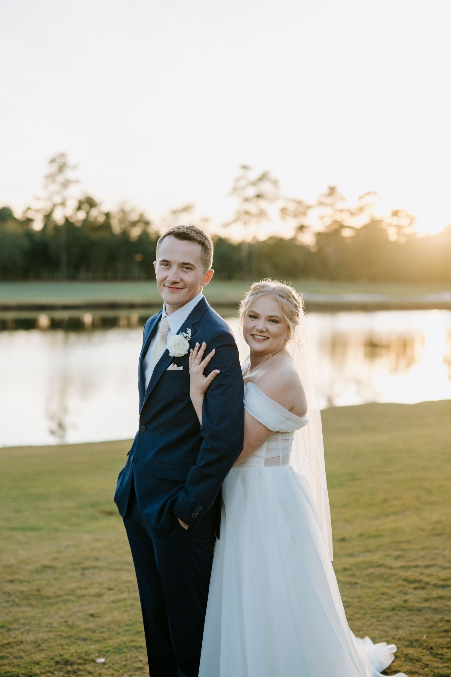 A romantic wedding photo series at sunset by a lake with a couple in formal attire.