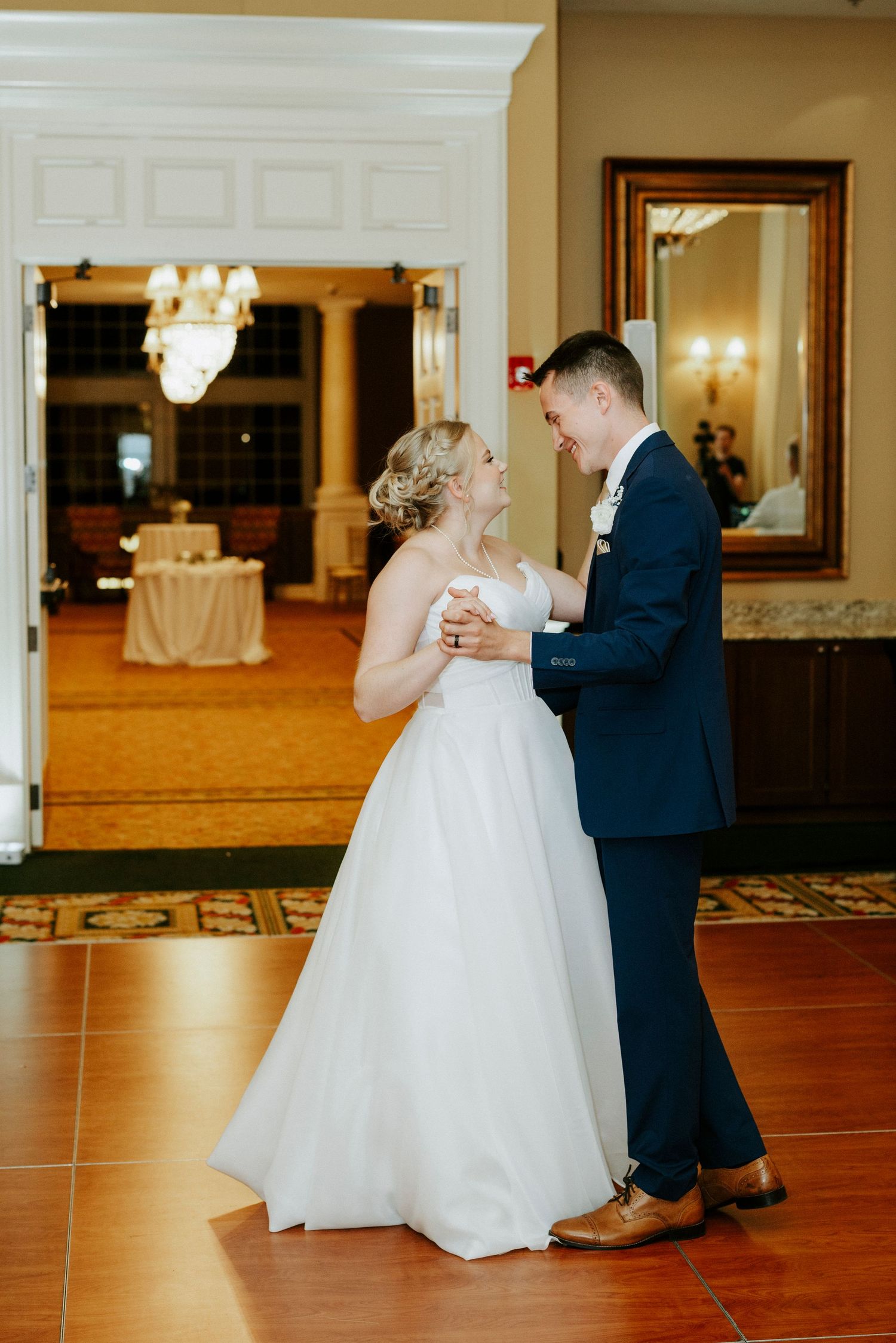 Couple performs their first dance on a polished wooden floor in an elegant ballroom setting.