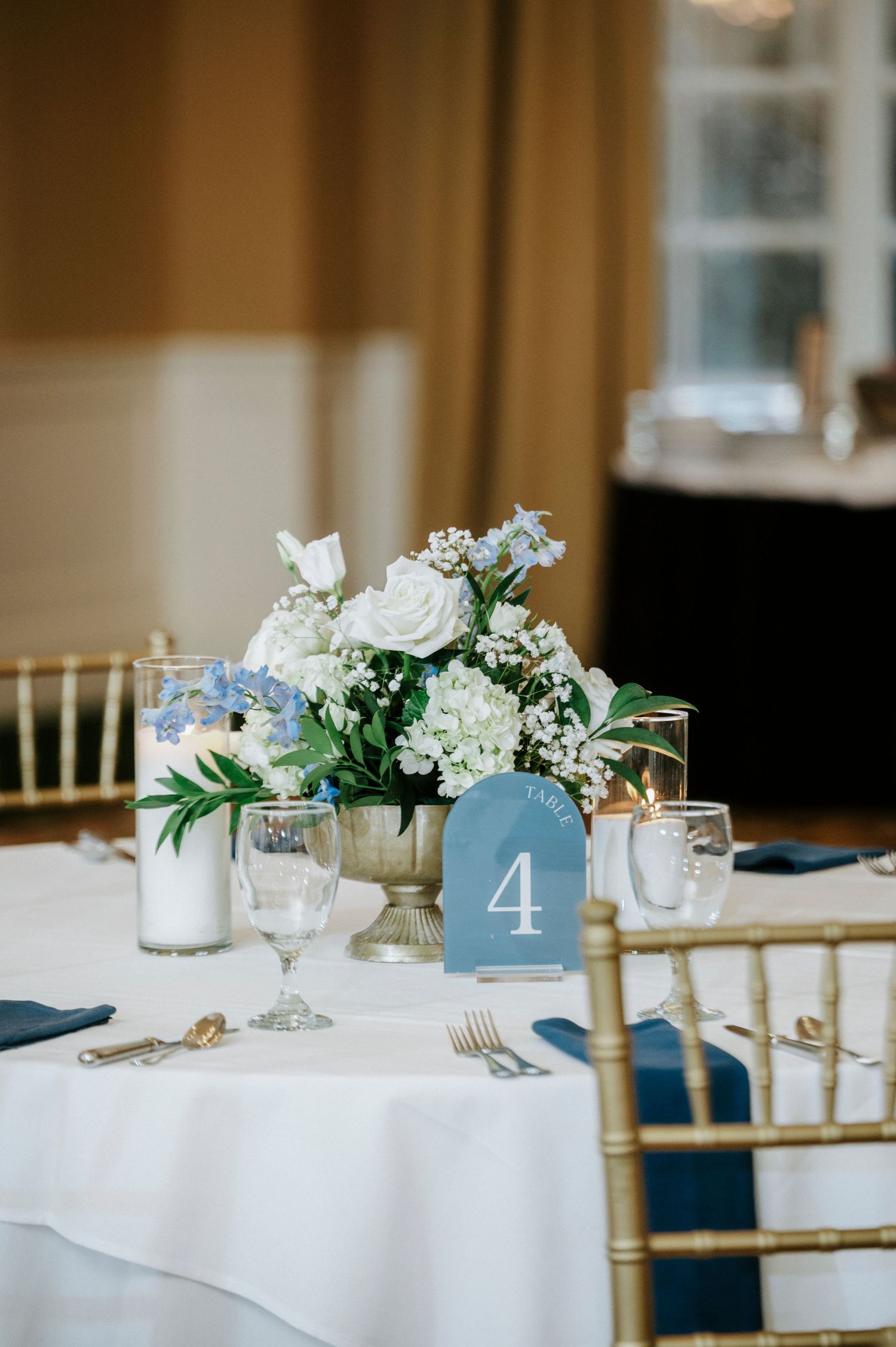 Elegant wedding reception tables with white linens, blue table numbers, and delicate floral centerpieces.