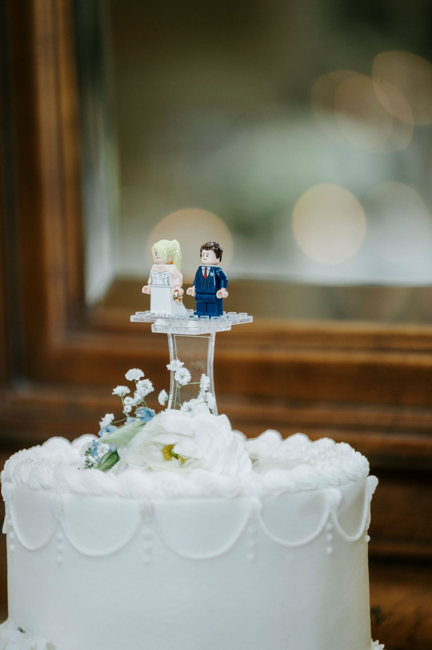 Close-up view of a white wedding cake decorated with delicate swirls and topped with miniature bride and groom figures.