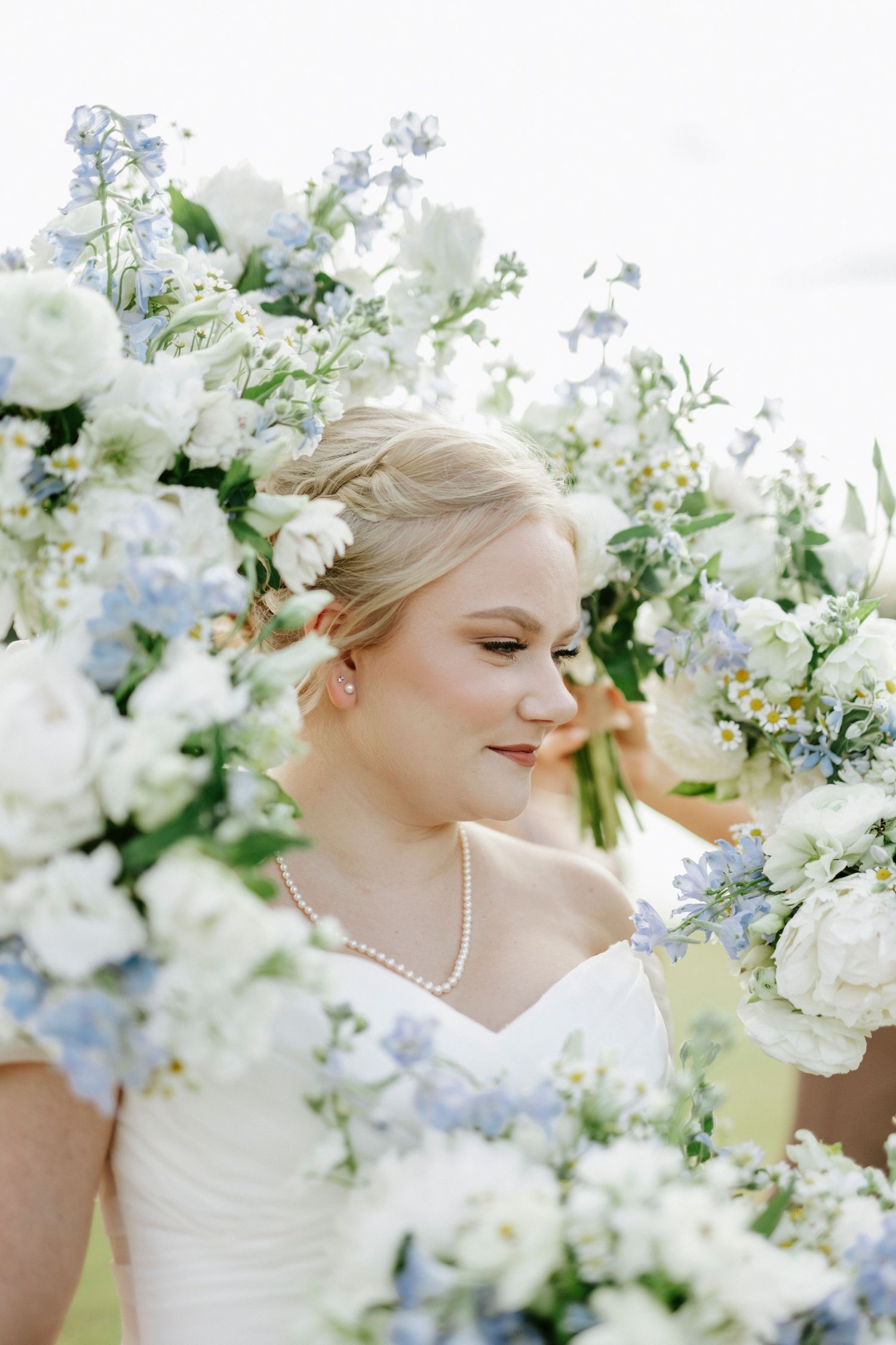 Bridal portrait surrounded by delicate white and blue floral arrangements in an outdoor garden setting.