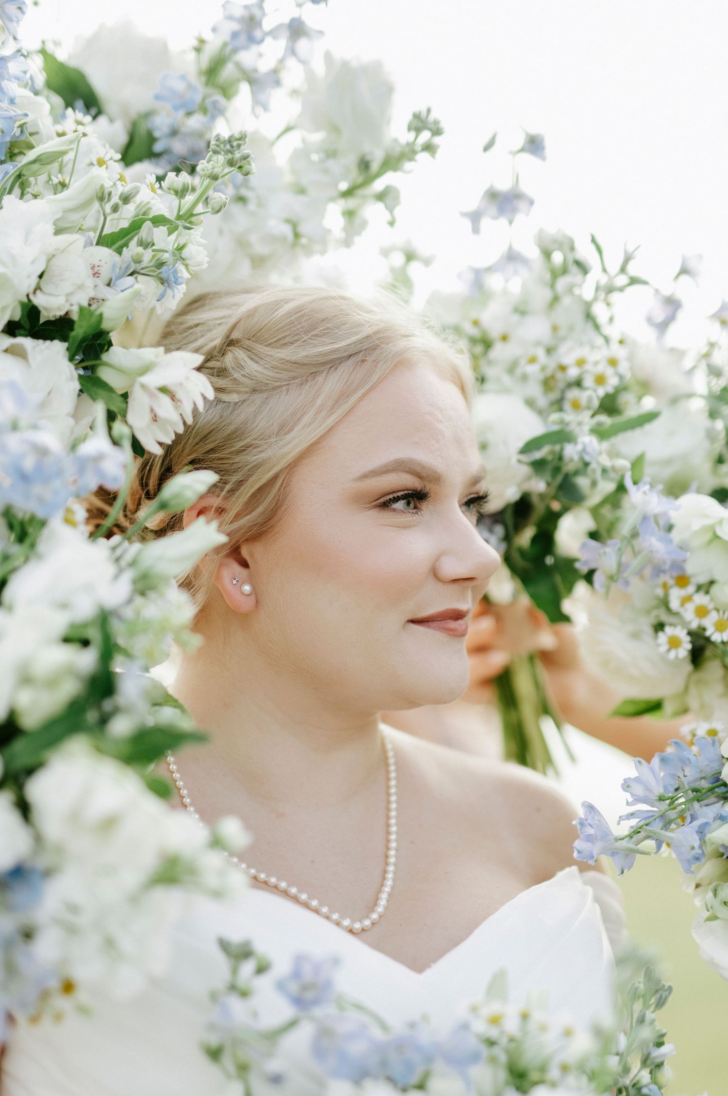 A romantic bridal portrait surrounded by delicate white and pale blue flowers with pearl necklace details.