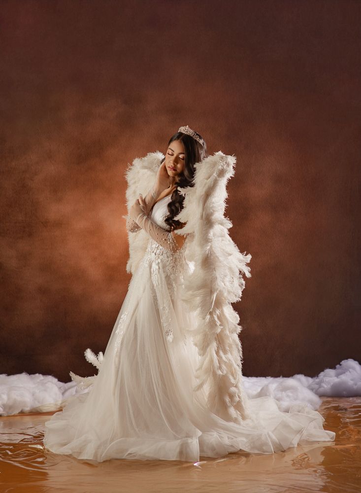 A bride in a flowing white dress with feather details twirls gracefully against a dark brown studio backdrop.