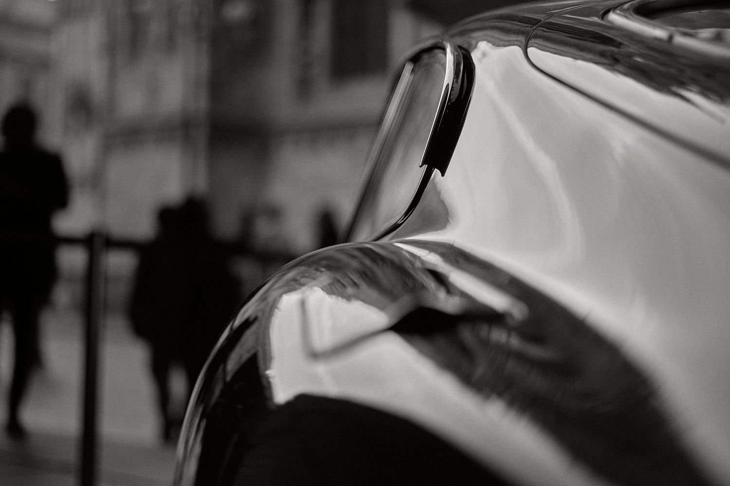 A row of cars parked on a city street with a mix of vintage and modern vehicles visible.
