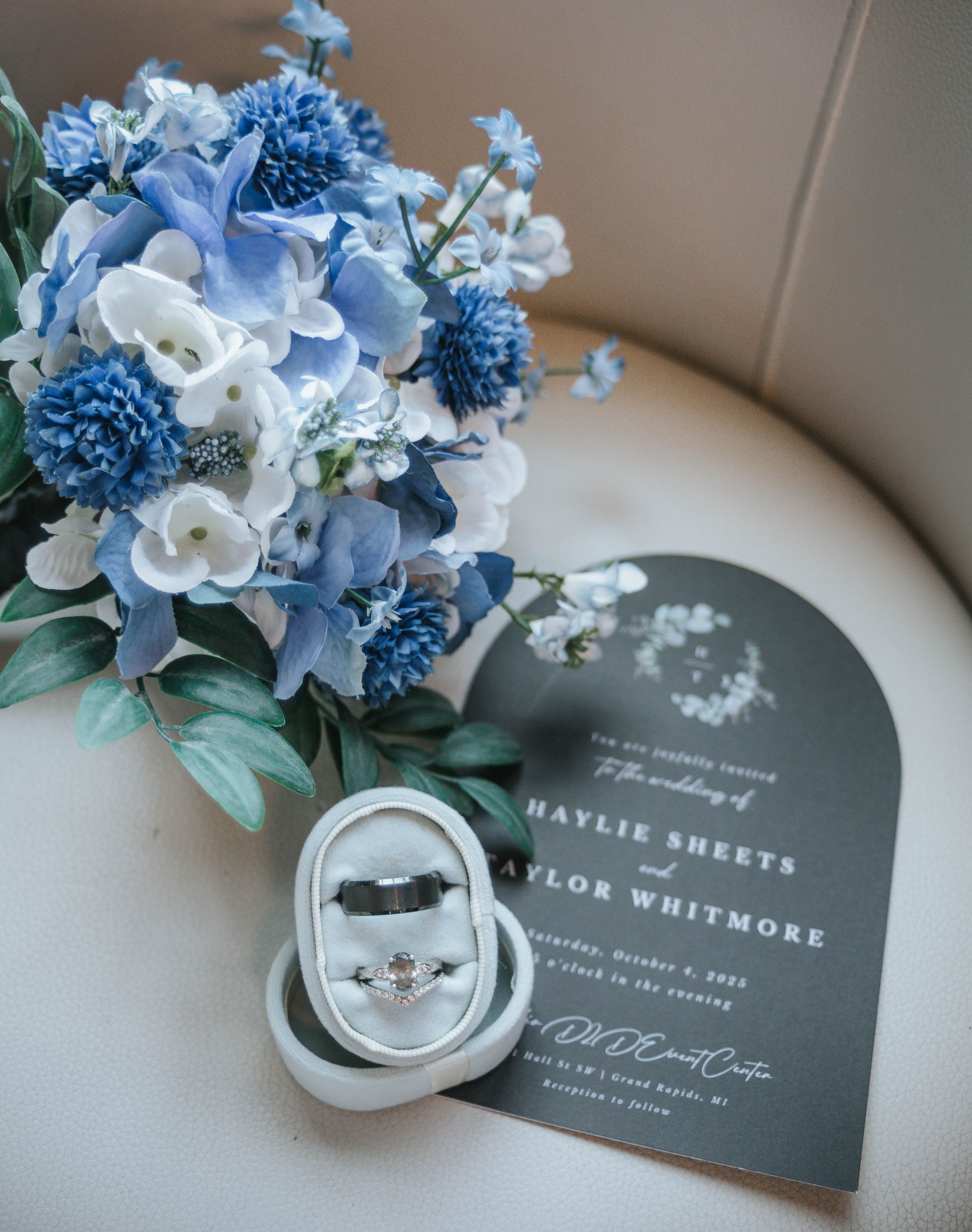 Wedding invitation and blue floral arrangement with white flowers sit elegantly on a light colored surface.