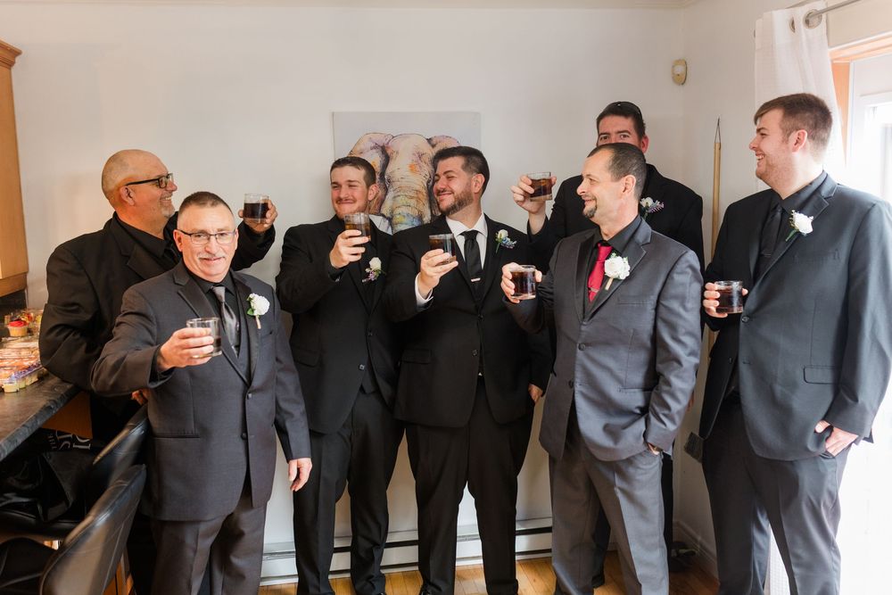A group in formal attire stands together laughing and sharing drinks during a celebratory moment.