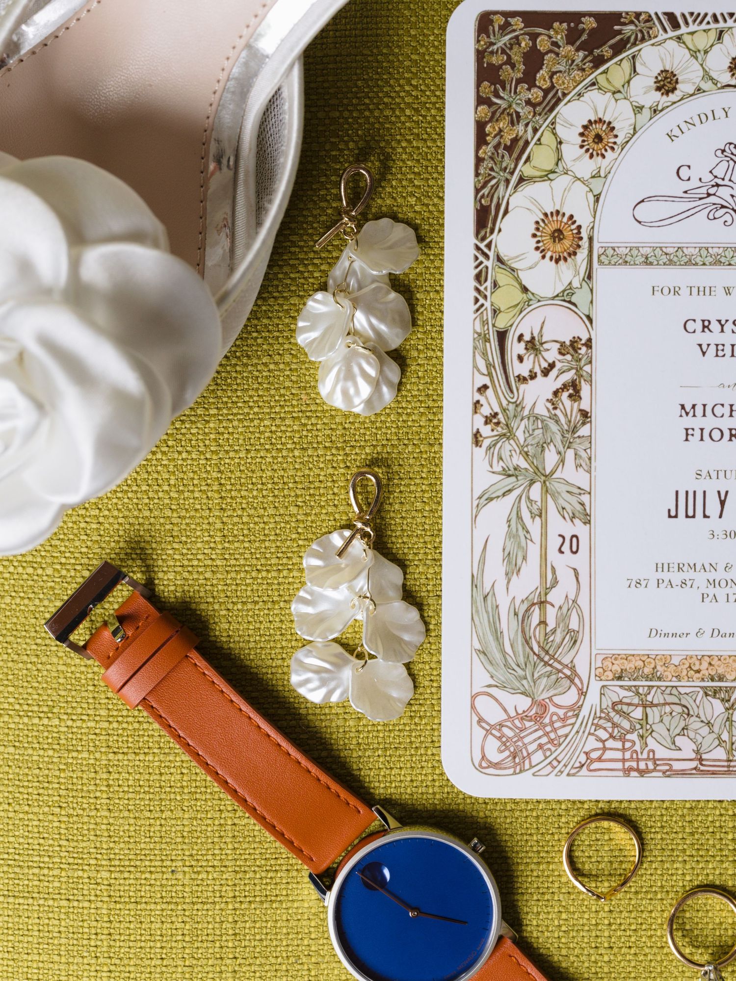 Wedding invitation details with blue watch and gold floral design on olive green background.