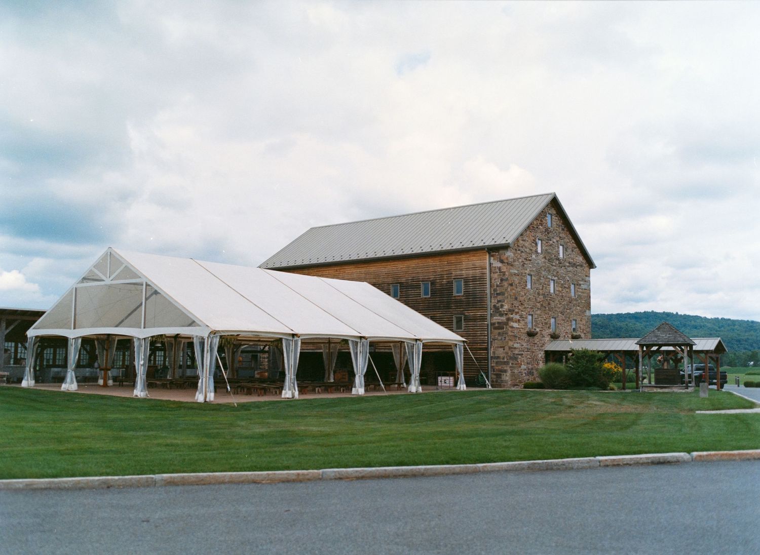 Rustic stone barn wedding venue with white tent pavilions set against rolling countryside landscape.