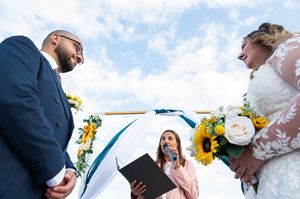 Wedding ceremony participants exchange vows under a bright blue sky with mountains in the background.