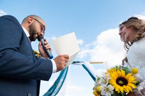 Wedding ceremony participants exchange handwritten vows while holding sunflower bouquet.