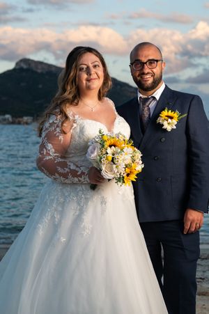 Seaside wedding portrait with sunflower bouquet against mountain backdrop.