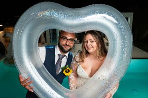 Couple poses through heart-shaped pool floats during nighttime celebration.