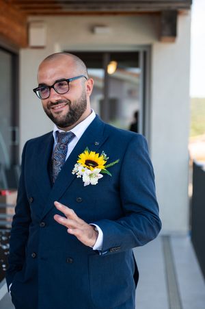Groomsman wearing a navy suit with sunflower boutonniere gestures expressively during outdoor wedding.
