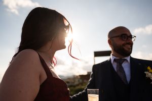 Silhouettes of wedding guests against bright sky during outdoor reception.