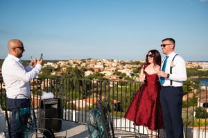 Wedding guests socializing on balcony overlooking Mediterranean town.