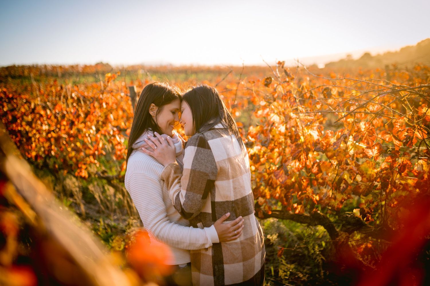 Two people embrace in a romantic moment surrounded by orange autumn foliage at golden hour.