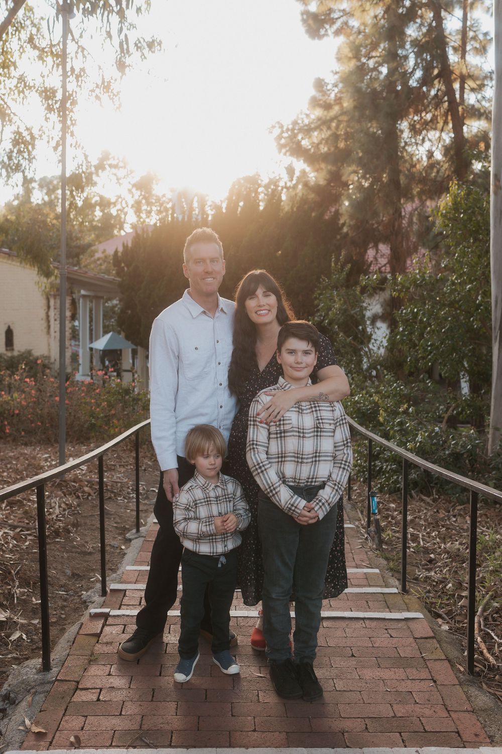 Family of four poses on brick steps during sunset in casual coordinated outfits.