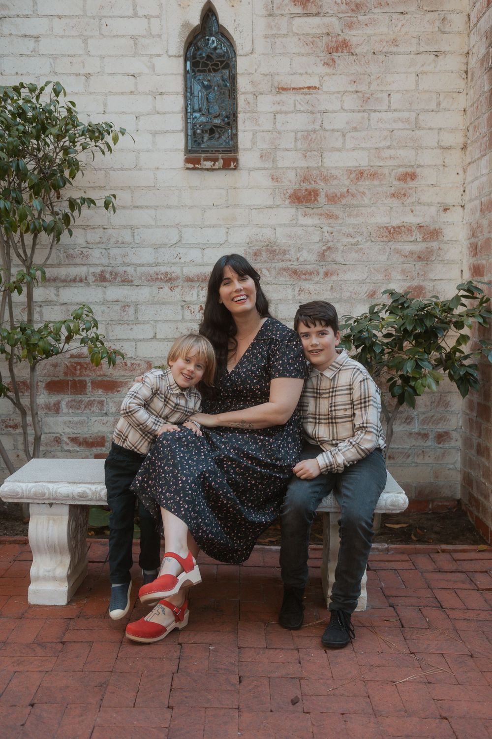 Portrait on brick patio with stone bench and ornate window detail in background.
