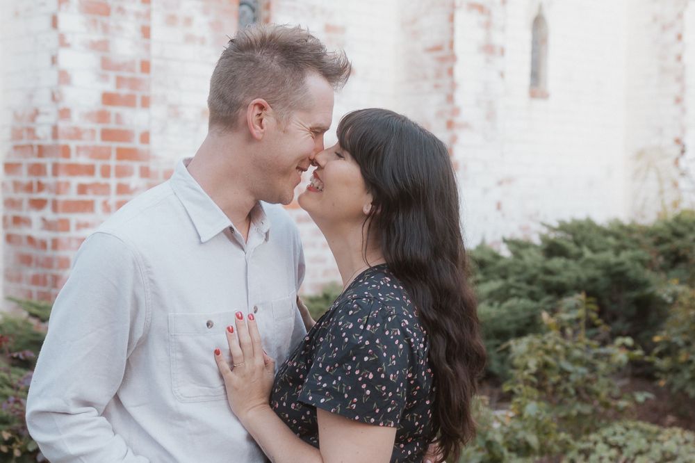 Intimate couple moment captured against weathered brick wall and garden setting.