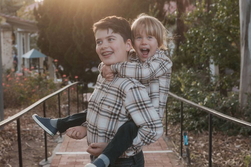 Playful siblings in matching plaid shirts laughing on outdoor steps.
