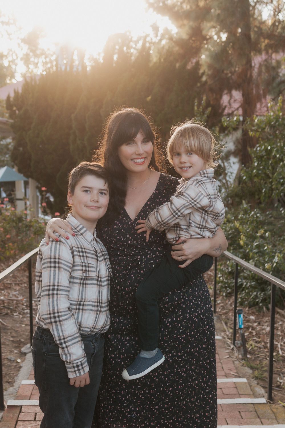 Family portrait on outdoor steps at sunset with coordinating plaid outfits.