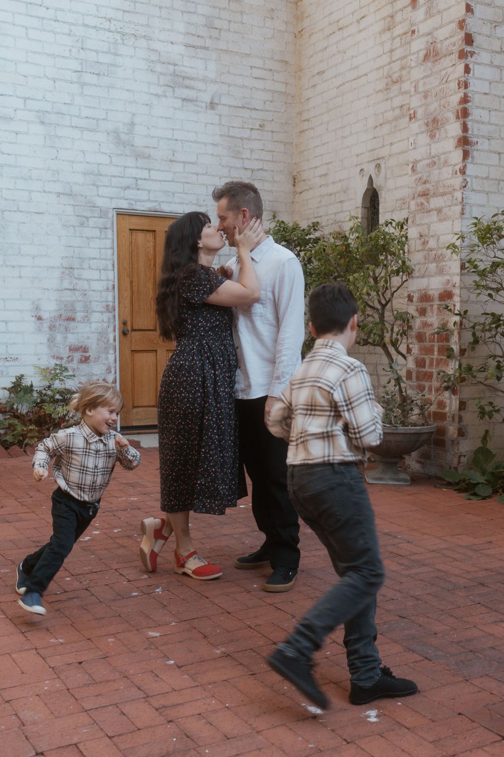 Family sharing candid moments on brick patio while children play around them.