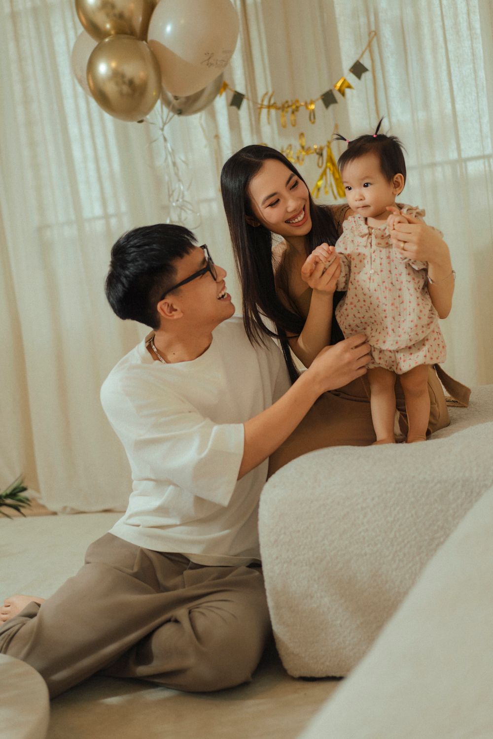 Family celebrates birthday with gold balloons and decorations in a cozy home setting.