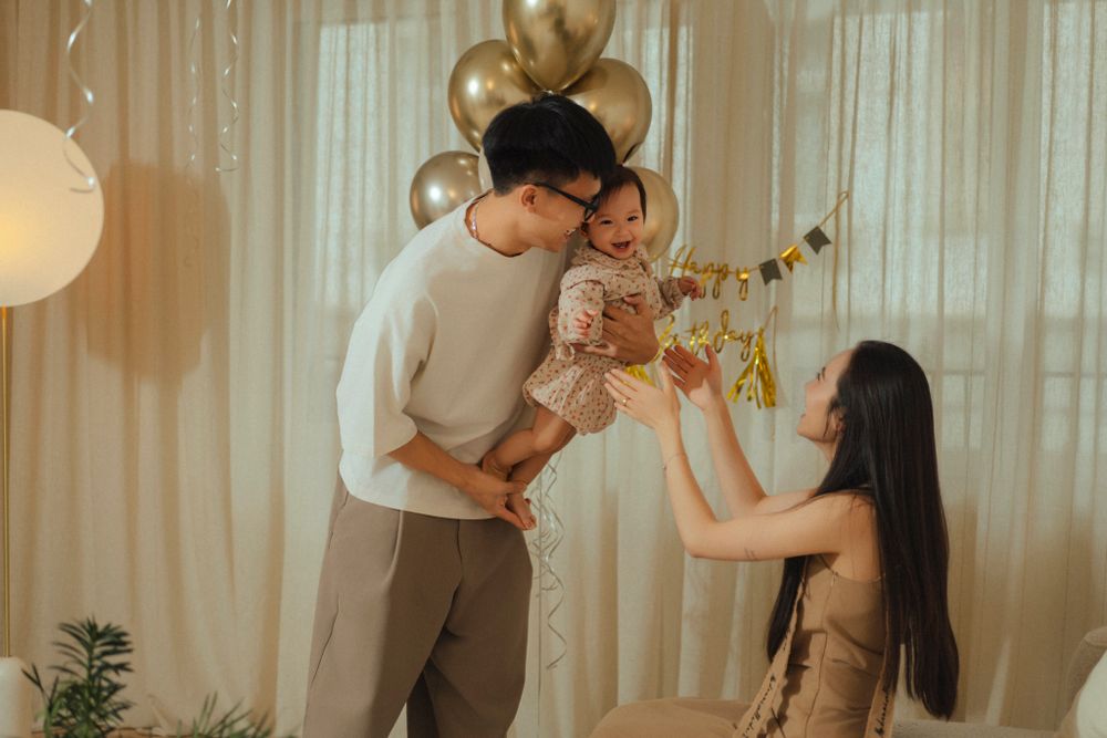 Family celebrating together with balloons and decorations in a cozy room with soft lighting and sheer curtains.