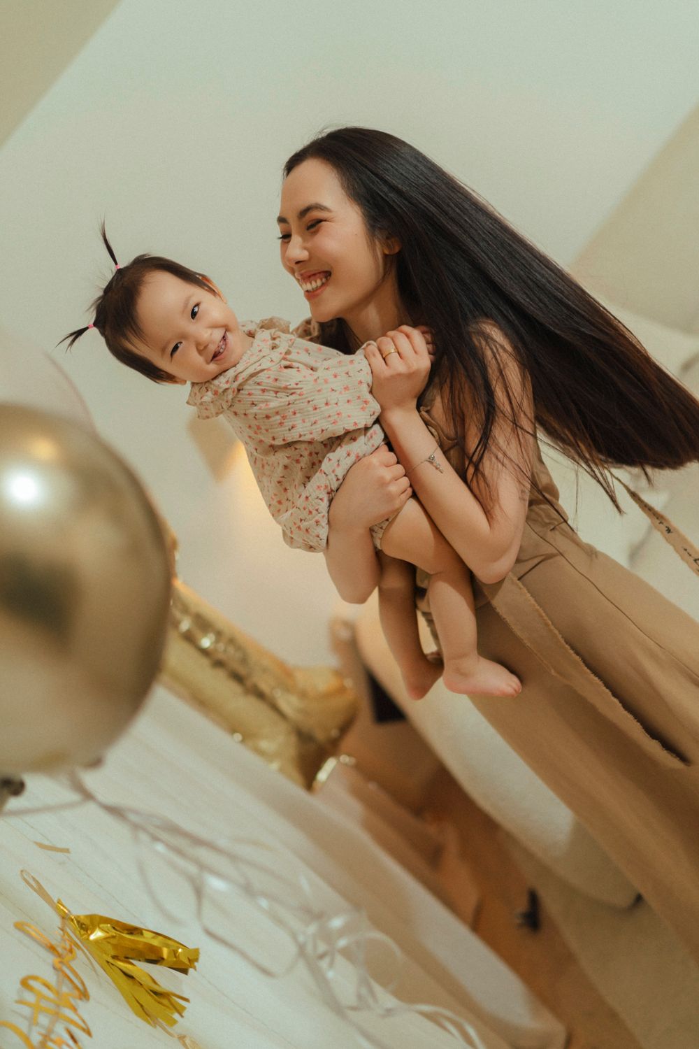 A parent and child share a joyful moment together with gold balloons in the background during a celebration.