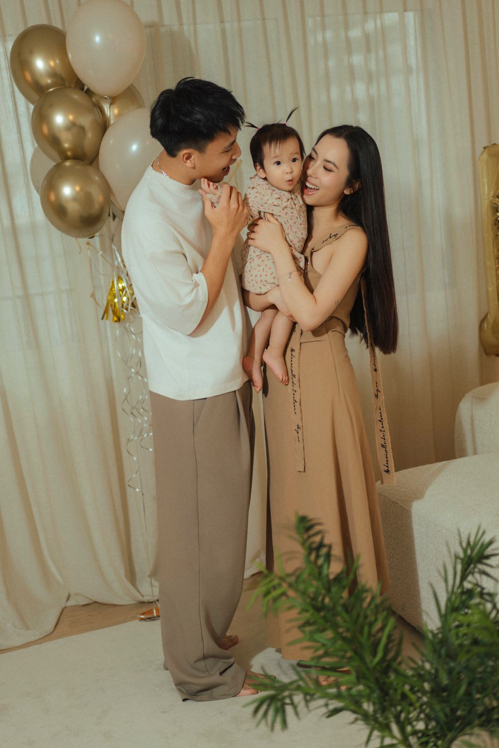 A family poses together at a celebration with gold and white balloons and decorative elements in the background.