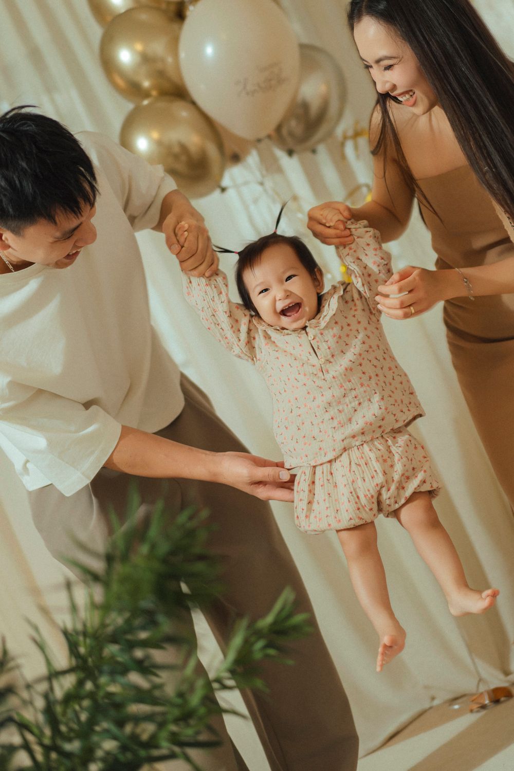 A joyful family moment with child lifted up in a room decorated with gold and white balloons.