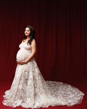 Stunning lace maternity dress with long train photographed against deep red curtain backdrop.