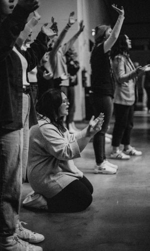 People raising hands in worship during a church service captured in black and white.