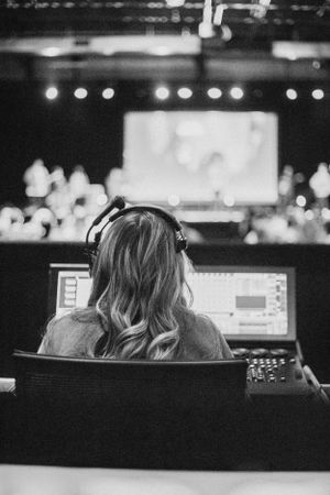 Sound engineer working at mixing console during live event with projection screen in background.