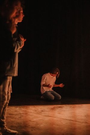 Two performers in dramatic poses on dimly lit stage with warm lighting.