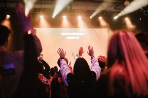Silhouetted crowd with raised hands at worship concert with bright stage lights.