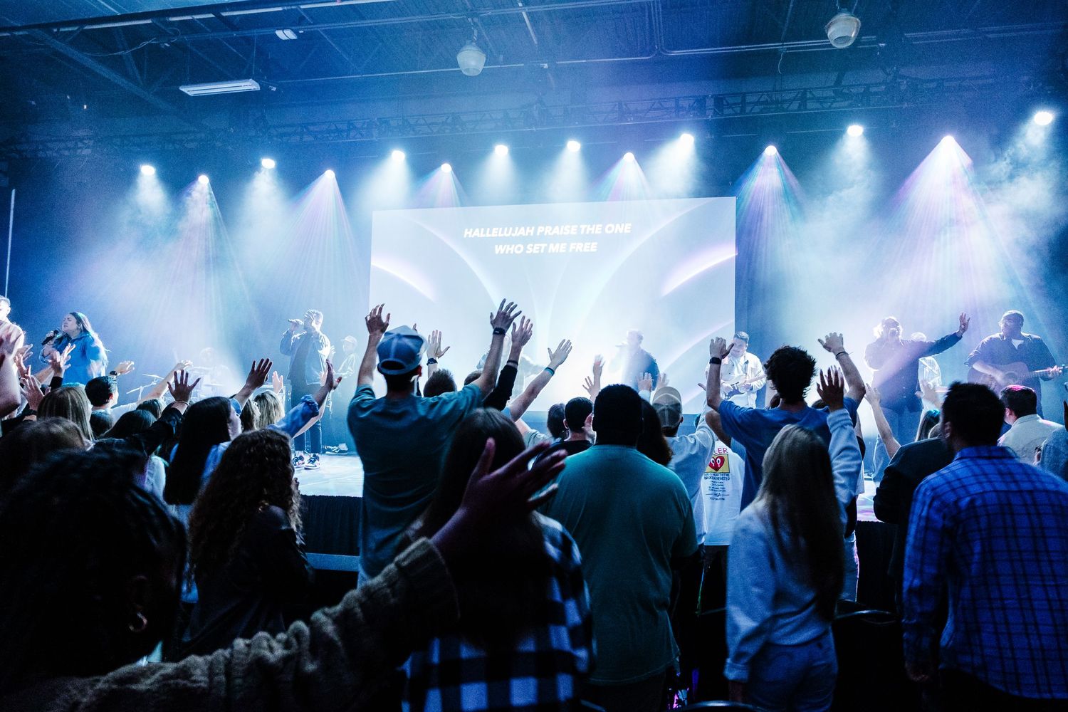 Energetic concert crowd with raised hands illuminated by blue stage lights during live performance.
