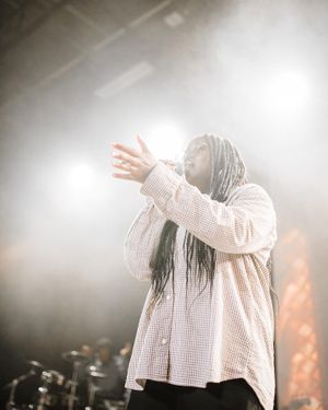A performer in a light-colored shirt singing passionately on stage amid dramatic lighting and fog effects.