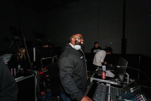 DJ working at a mixing board in a dark setting wearing winter clothing.