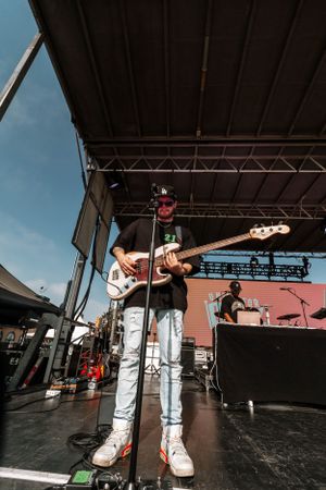 Bass guitarist performing on outdoor stage during daytime concert against blue sky.