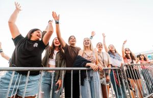 Excited fans cheering behind concert barriers at an outdoor event.
