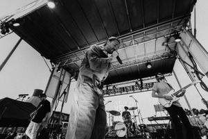 Wide angle black and white shot of band performing on outdoor festival stage.