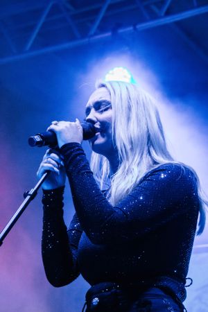 Singer performing on stage illuminated by blue lighting in sparkly dark outfit.
