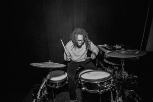 Black and white photo of drummer performing intensely behind drum kit on dark stage.