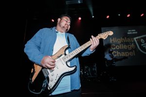 A guitarist performs on stage with blue lighting and plays an electric Stratocaster guitar.